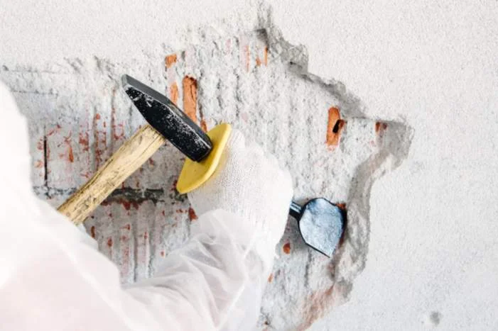 Hand mit Hammer entfernt Putz von Wand